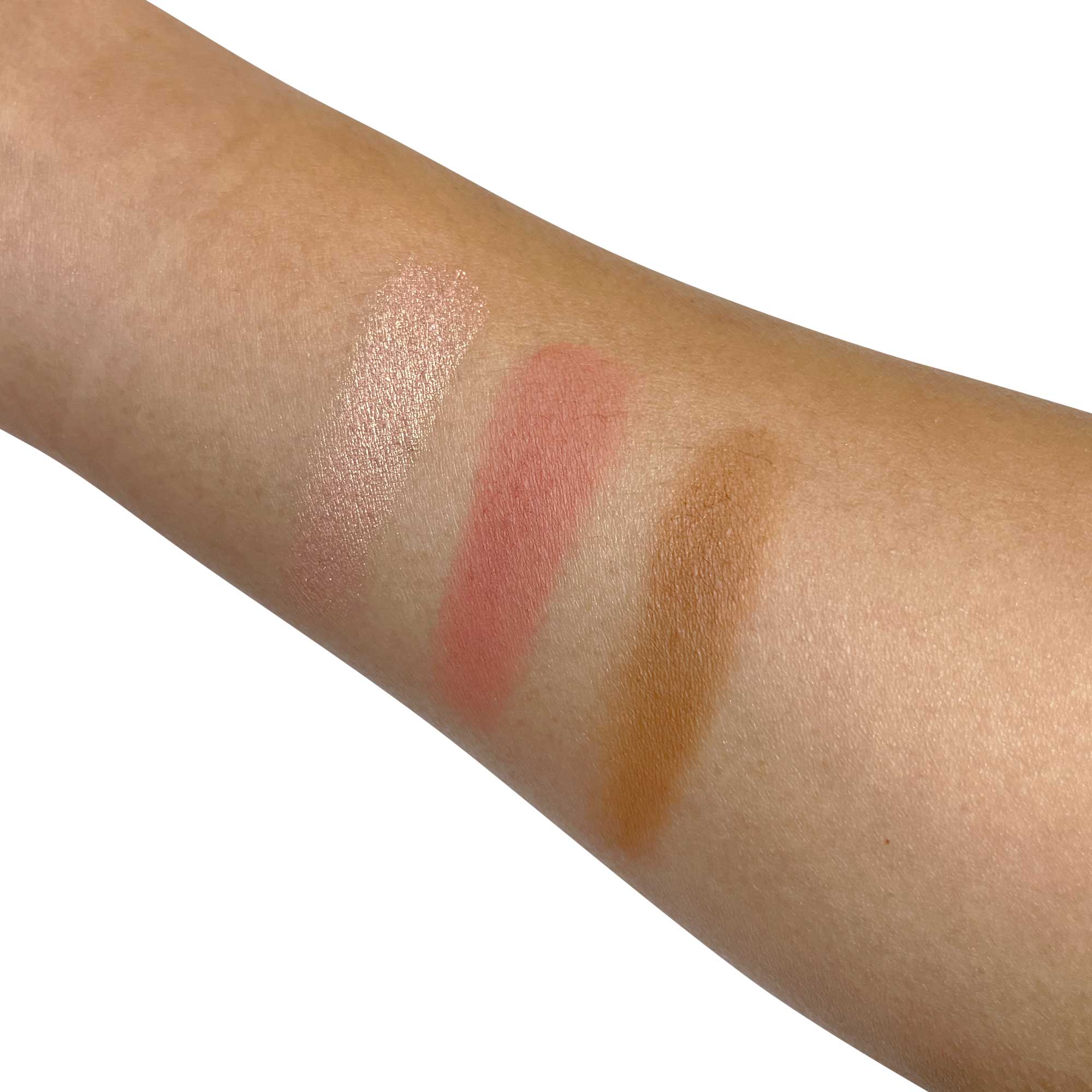 Three swatches of a cheek palette are shown on an arm: a shimmery highlight, a matte peach blush, and a matte brown contour.