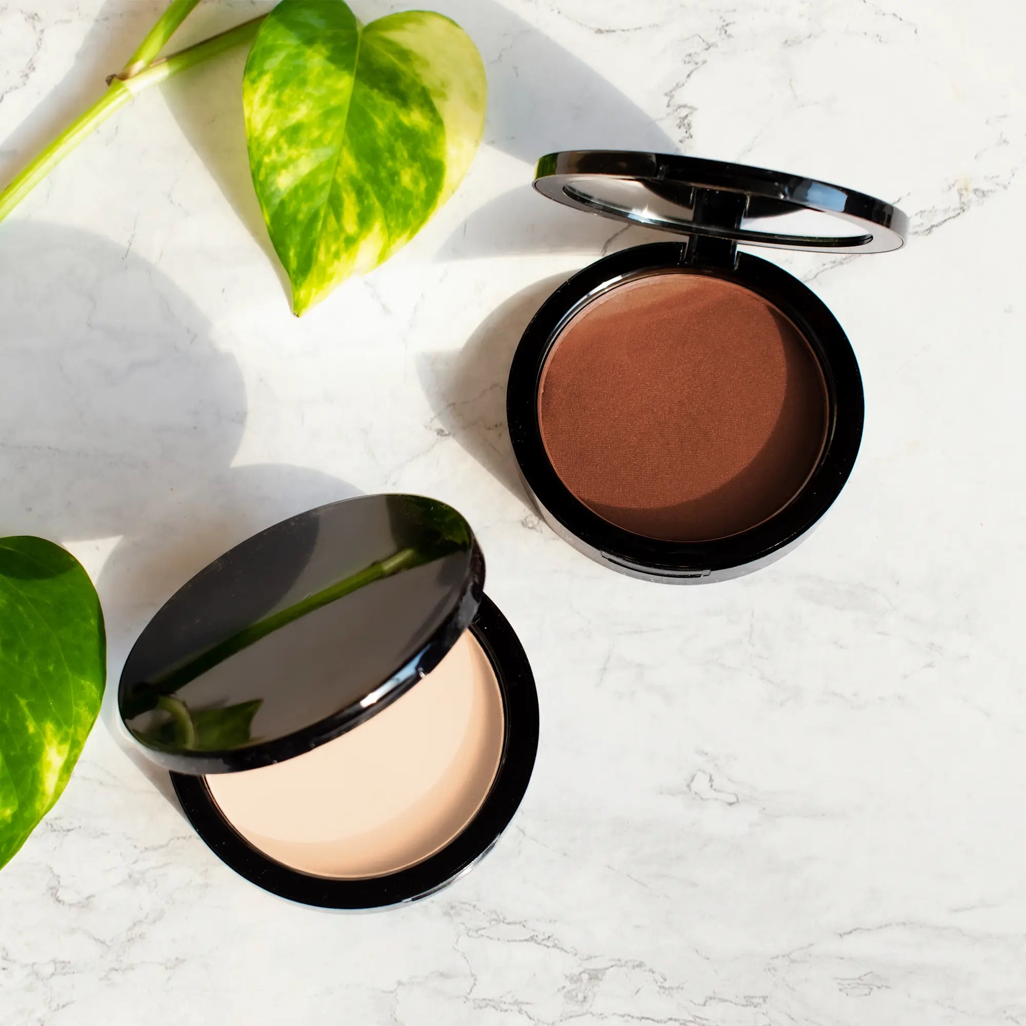 Two open compacts of powder foundation, one light and one dark, on a marble surface.