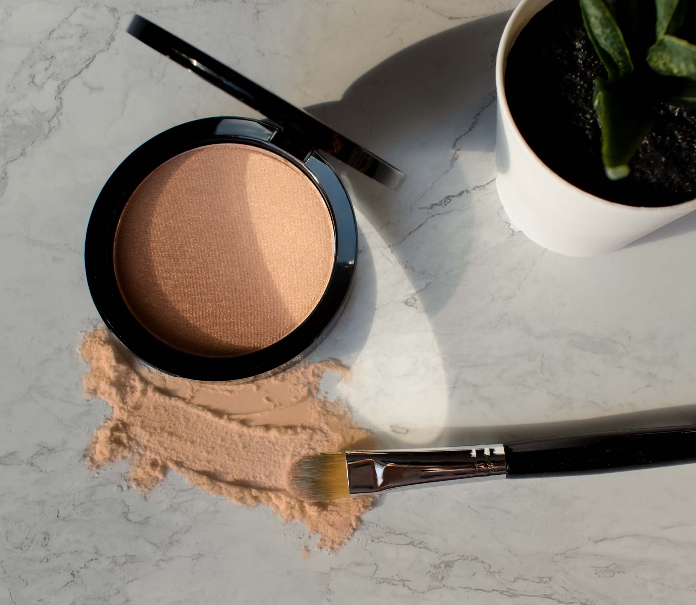A compact of luminizing powder with a brush and spilled powder on a marble surface.