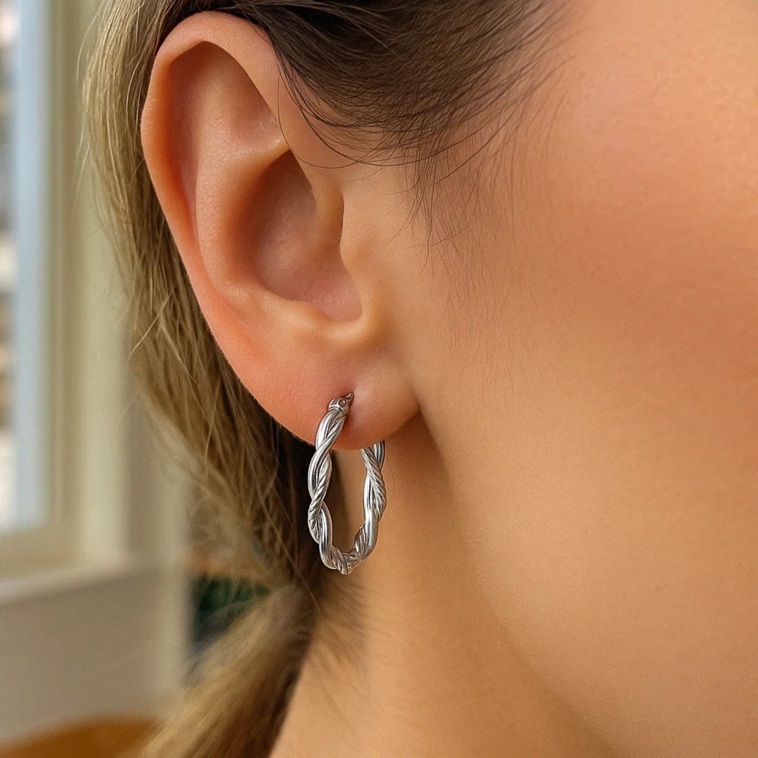 Sterling silver oval hoop braided diamond cut earrings on a person's ear.