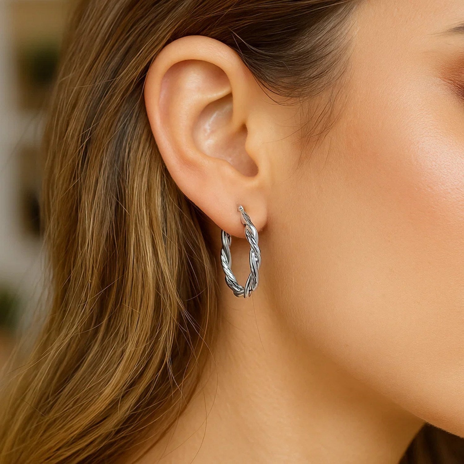 Sterling silver oval hoop braided diamond cut earrings on a woman's ear.