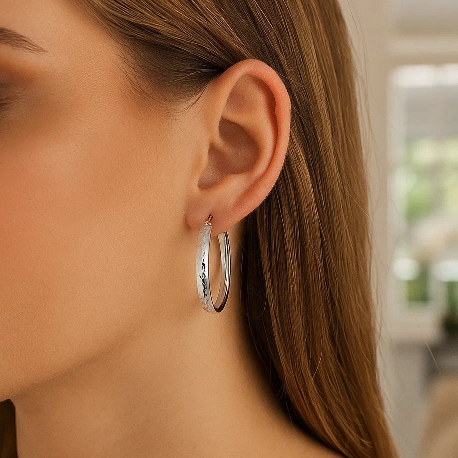 Sterling silver hammered hoop earrings with rhodium plating on a model's ear.