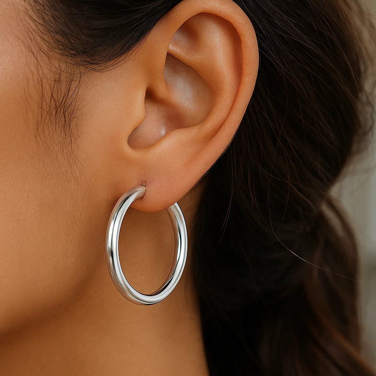 A close-up of an ear wearing a thick, polished silver hoop earring.