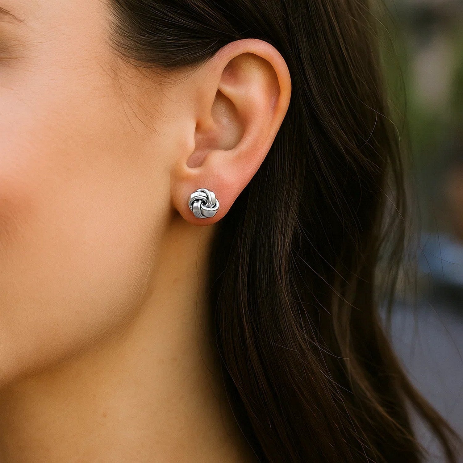 Petite sterling silver polished love knot earrings on a woman's ear.