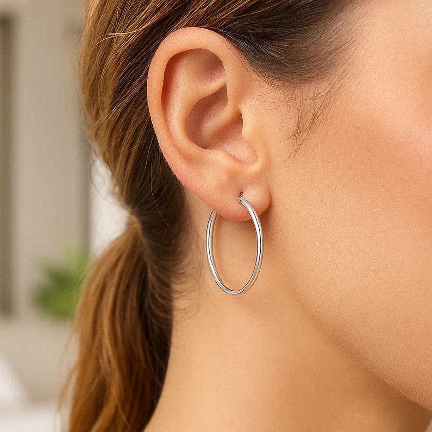 A woman wears a single sterling silver thin polished hoop earring.