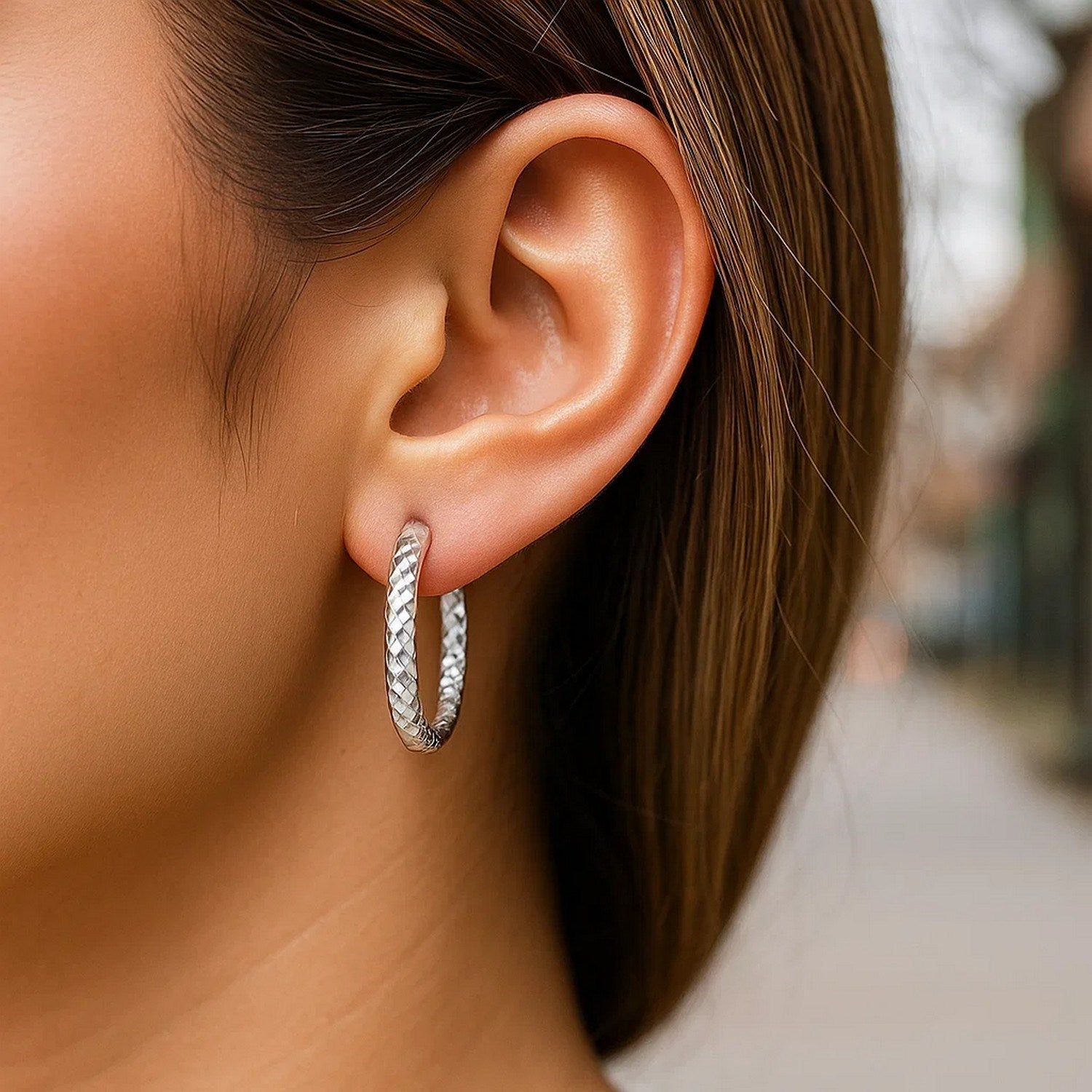 A woman wears a sterling silver faceted hoop earring with rhodium plating.