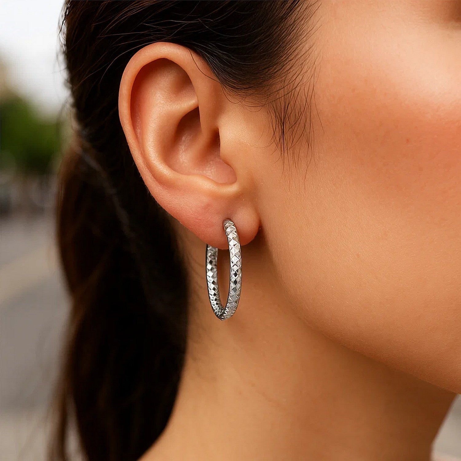 Sterling silver faceted hoop earrings with rhodium plating on a woman's ear.