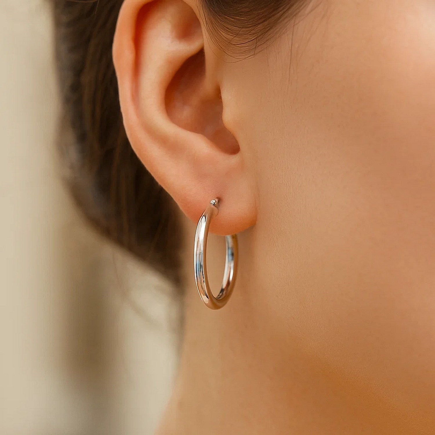 A woman wears a single polished sterling silver hoop earring with rhodium plating.