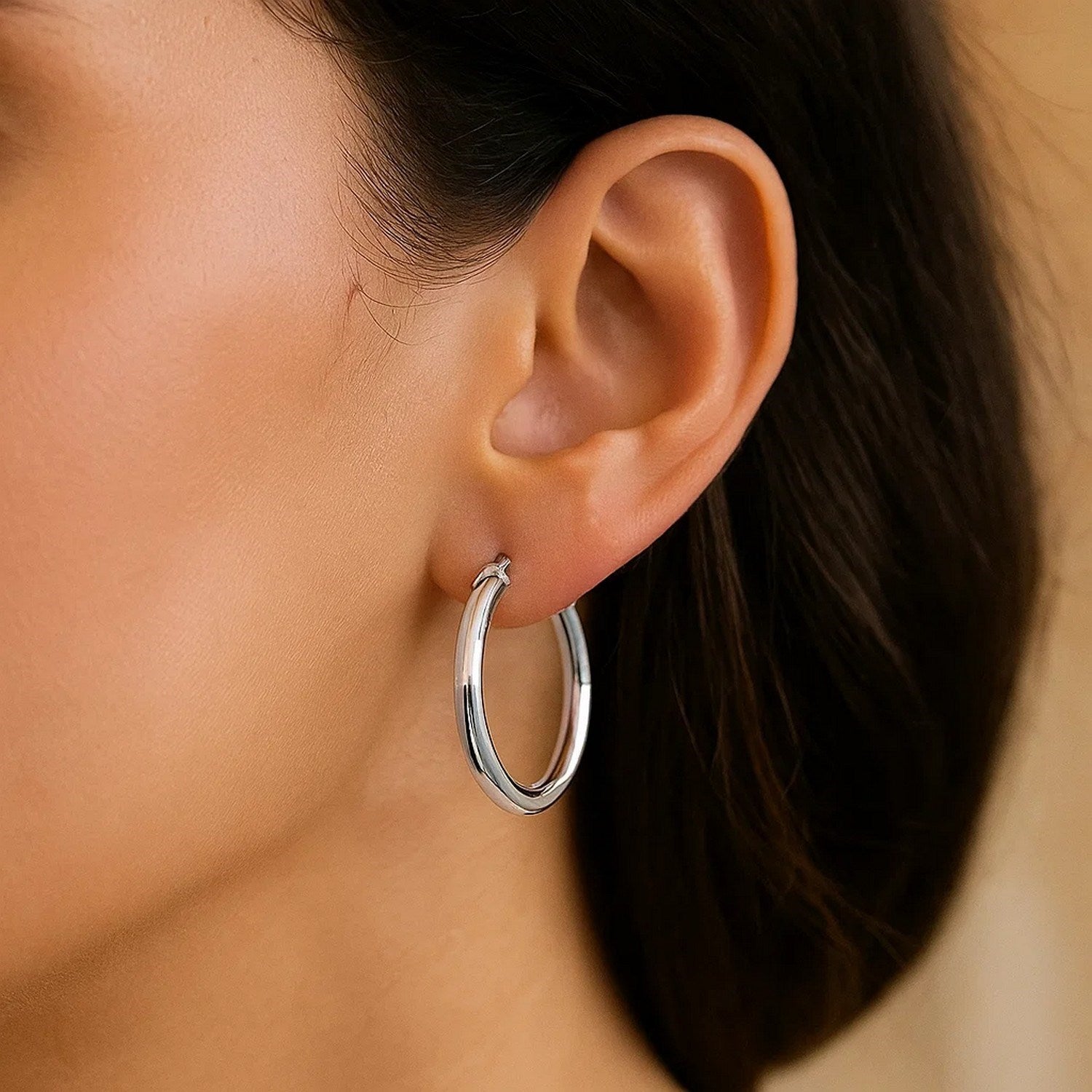 Sterling silver polished hoop earrings with rhodium plating on a person's ear.