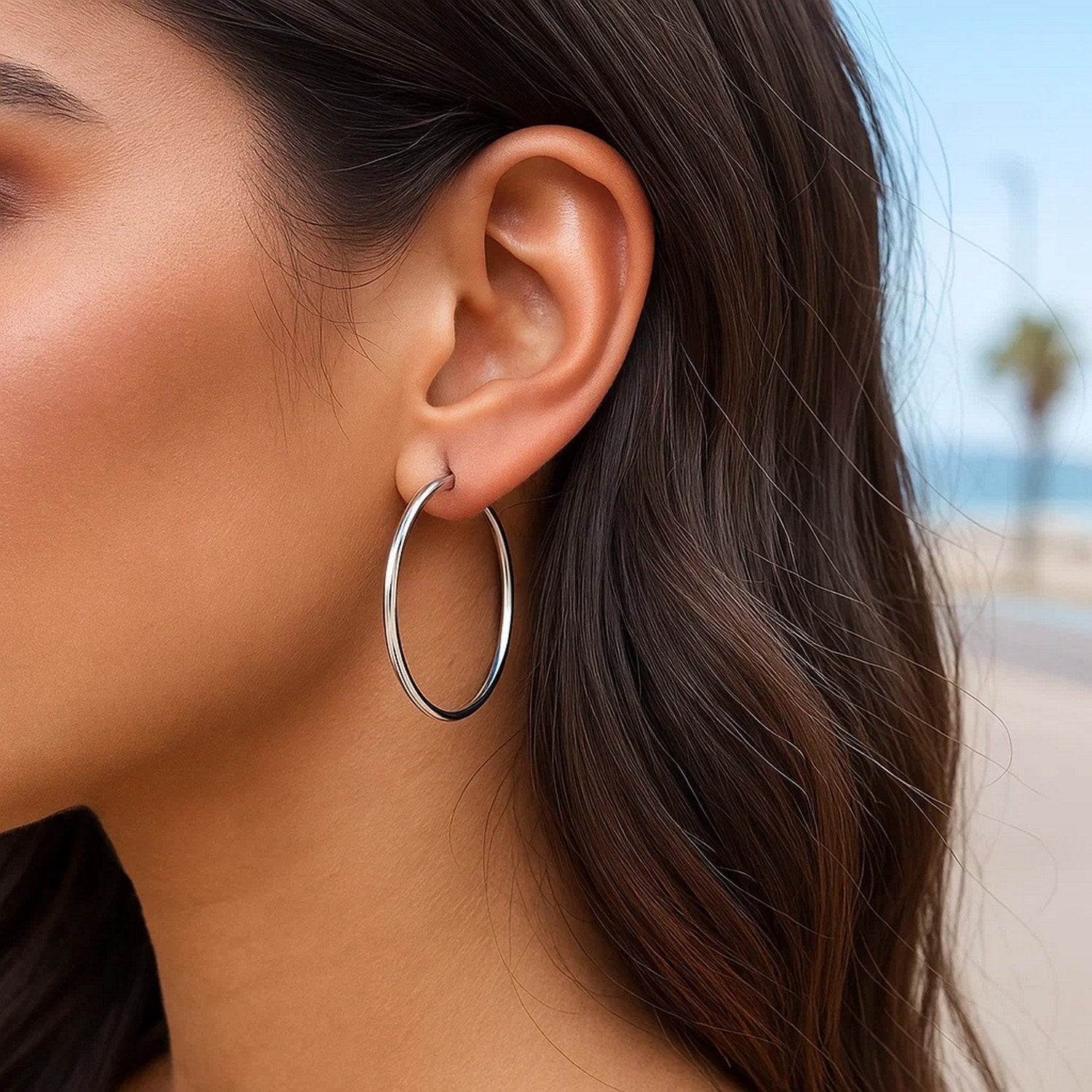 Sterling silver rhodium plated thin and polished hoop earrings on a woman's ear.