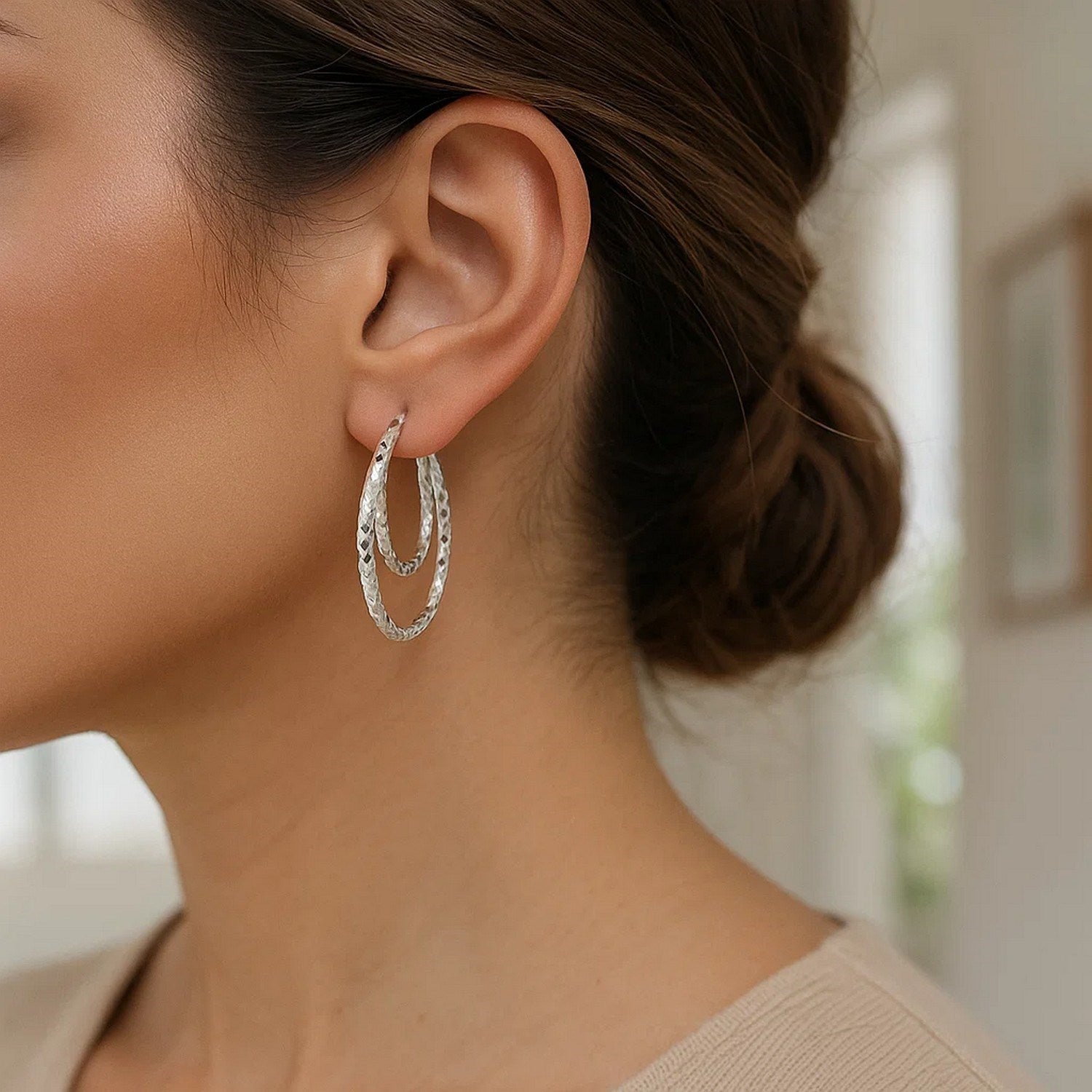 Sterling silver double oval textured hoop earrings on a woman's ear.