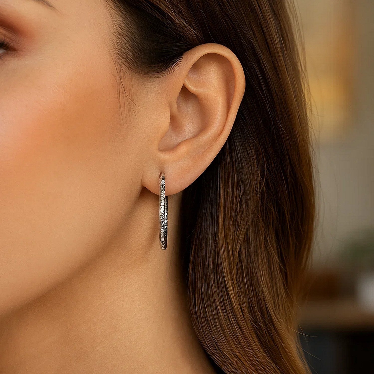 Sterling silver rhodium-plated woven style polished hoop earrings on a woman's ear.
