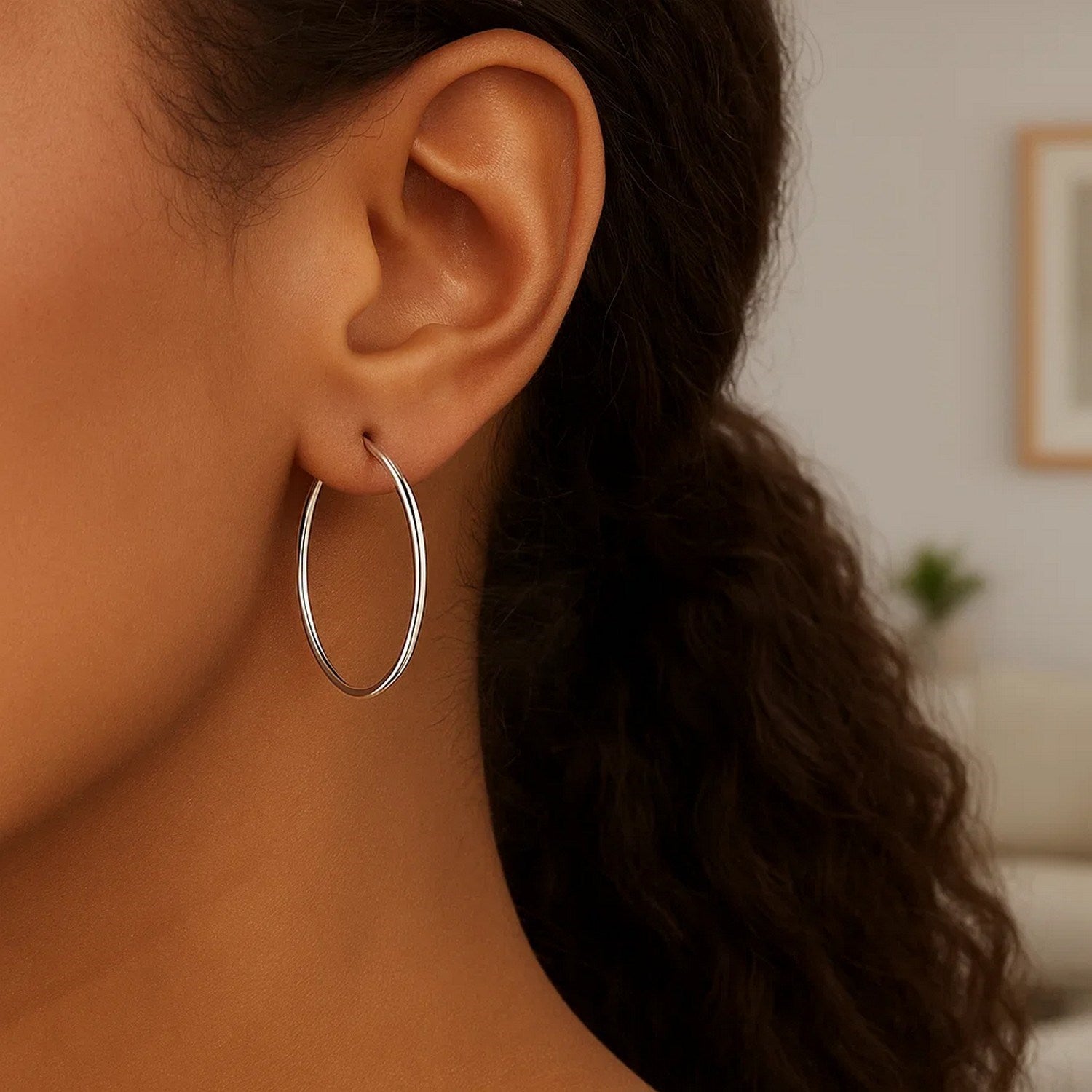 Sterling silver rhodium plated thin large polished hoop earrings on an ear.