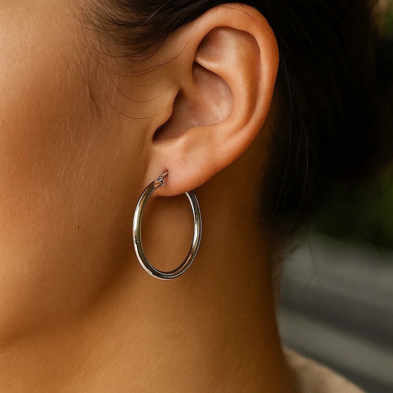Sterling silver rhodium plated polished hoop earring on an ear.