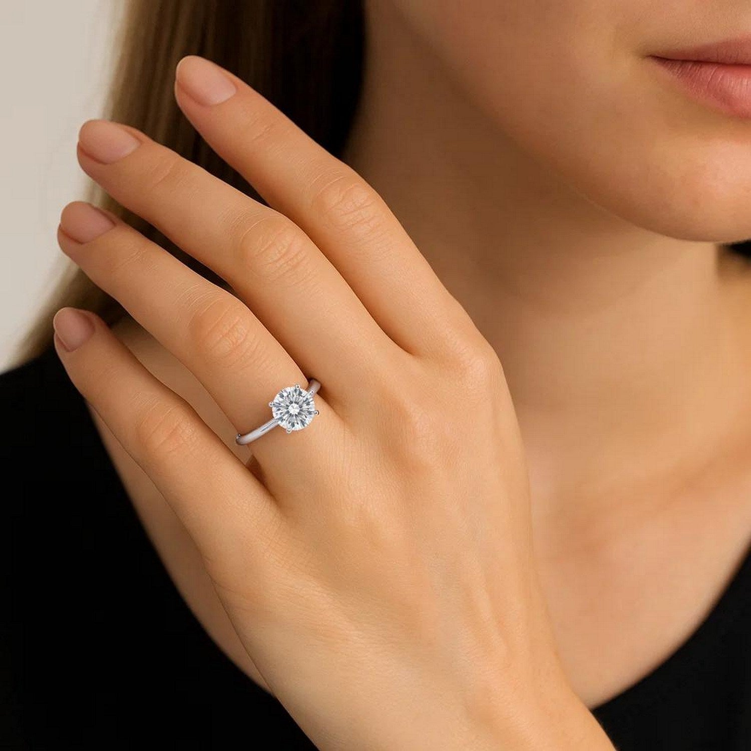 A woman's hand wears a sterling silver solitaire ring with a 2 carat round diamond.