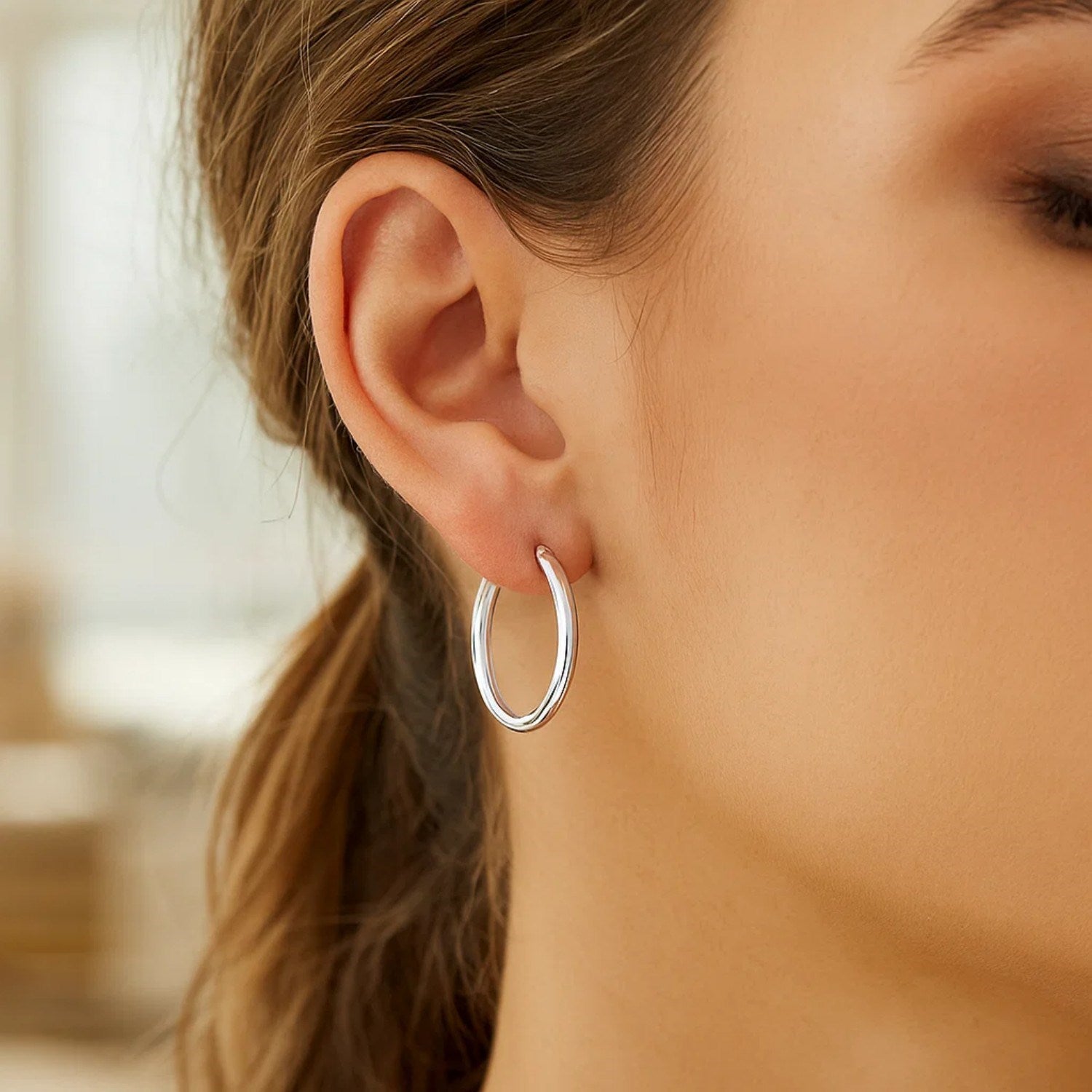 Sterling silver rhodium plated polished hoop earrings on a woman's ear.