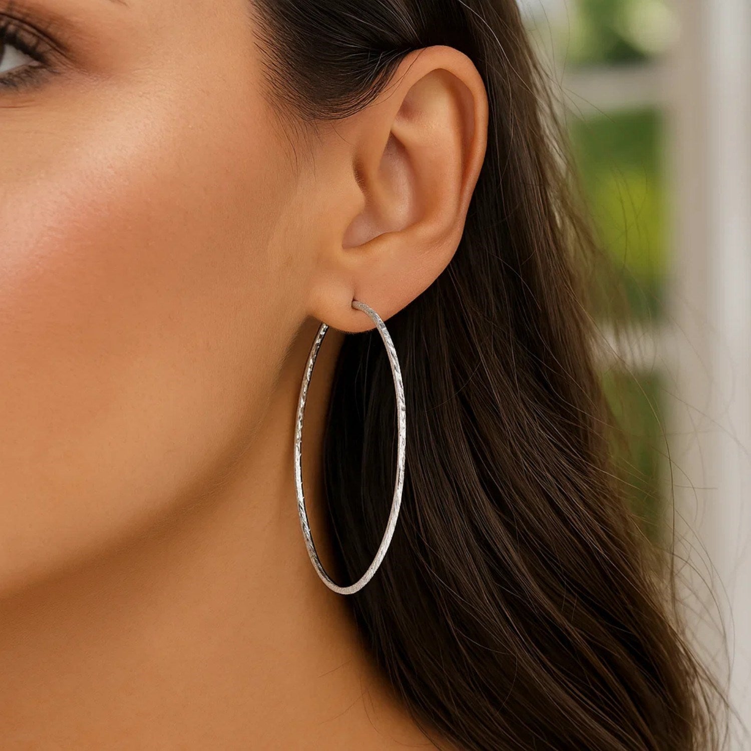 Sterling silver large textured round hoop earrings are worn on a woman's ear.