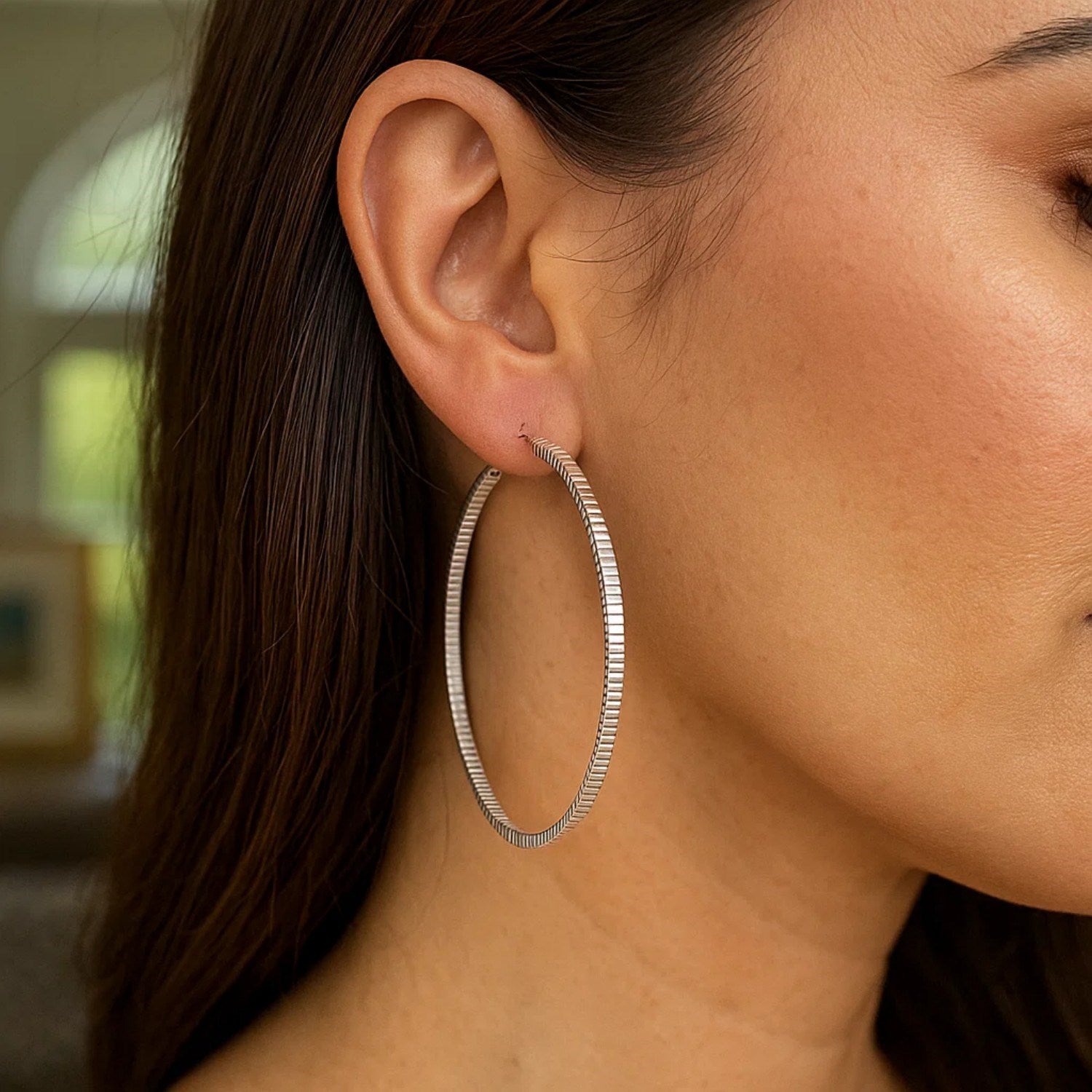 Sterling silver ridge textured hoop earrings on a woman's ear.
