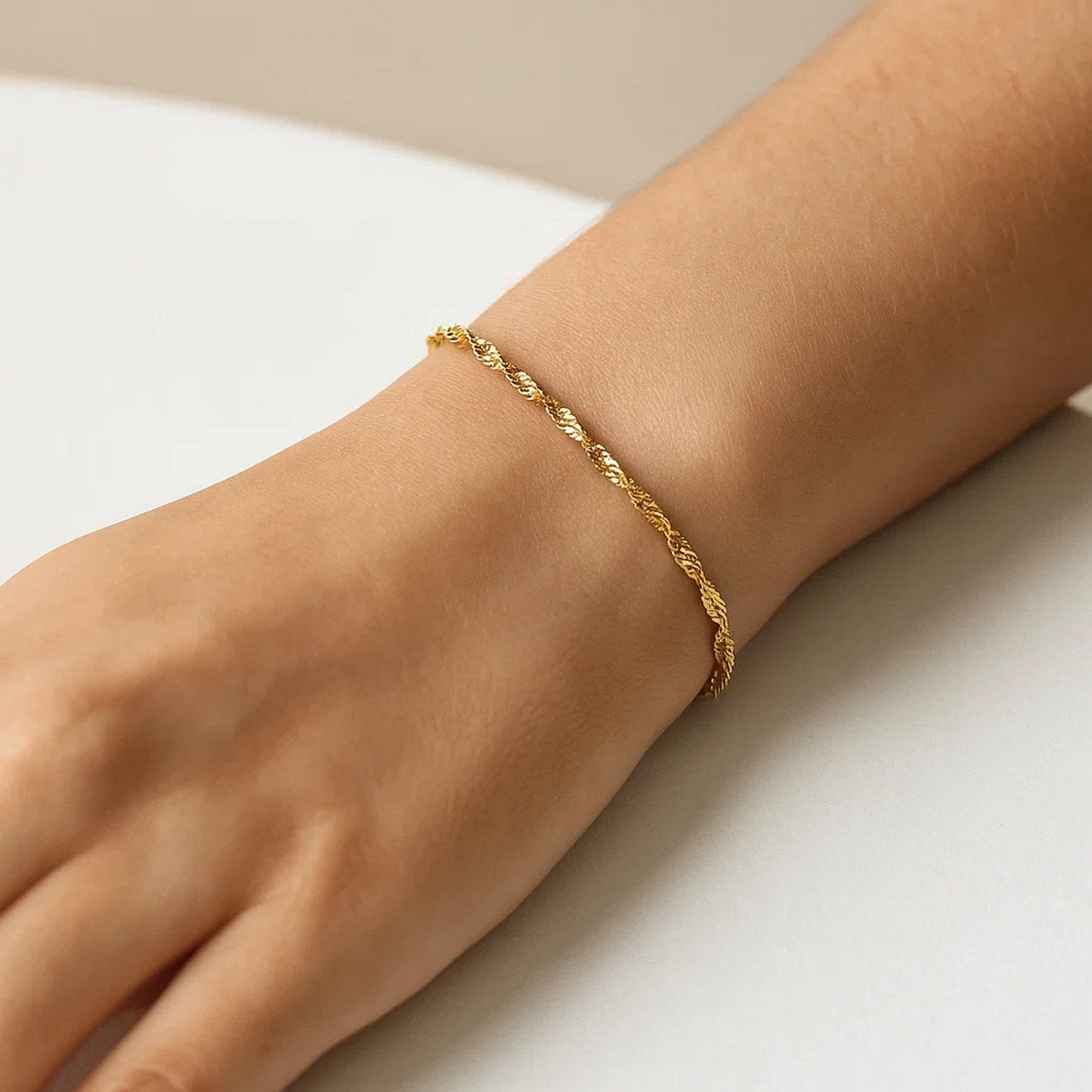 A 10k yellow gold Singapore bracelet with a spring ring clasp on a person's wrist.