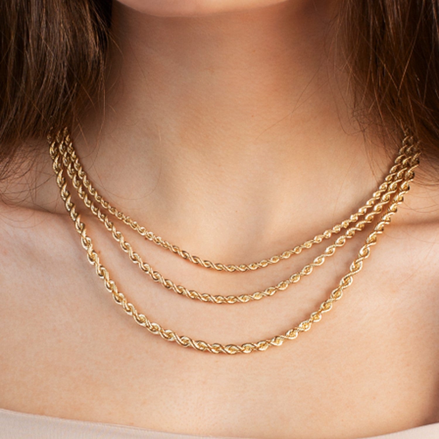 Three layered 14k yellow gold light rope chains on a person's neck.
