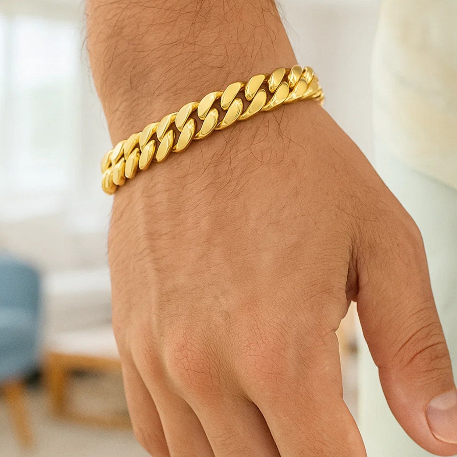 A man's arm and hand display a thick, shiny 14k yellow gold Miami Cuban bracelet.