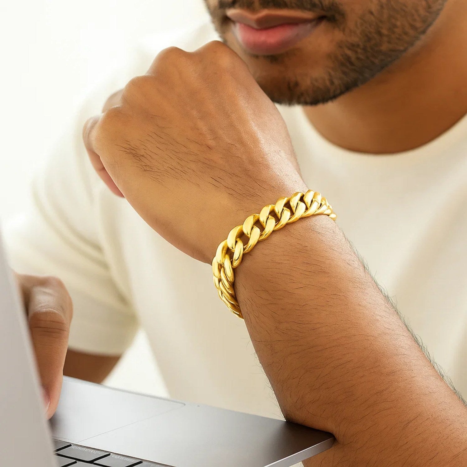 A man wears a thick, semi-solid 14k yellow gold Miami Cuban bracelet.