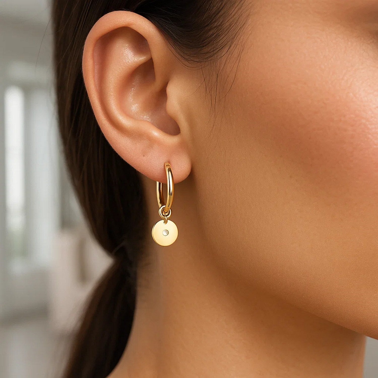14K yellow gold hoop earrings with diamond disc charms on a person's ear.