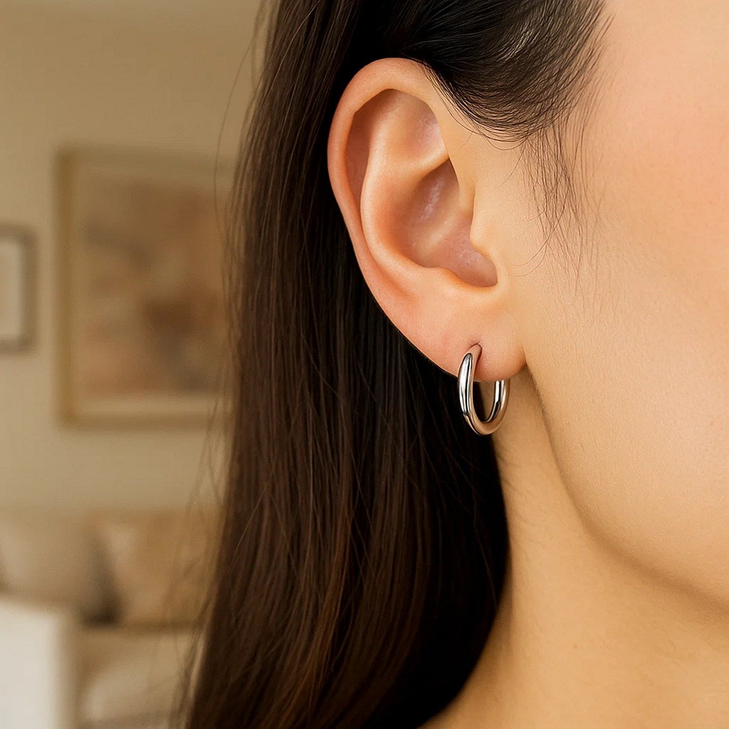 Sterling silver polished hoop earrings with rhodium plating on a woman's ear.