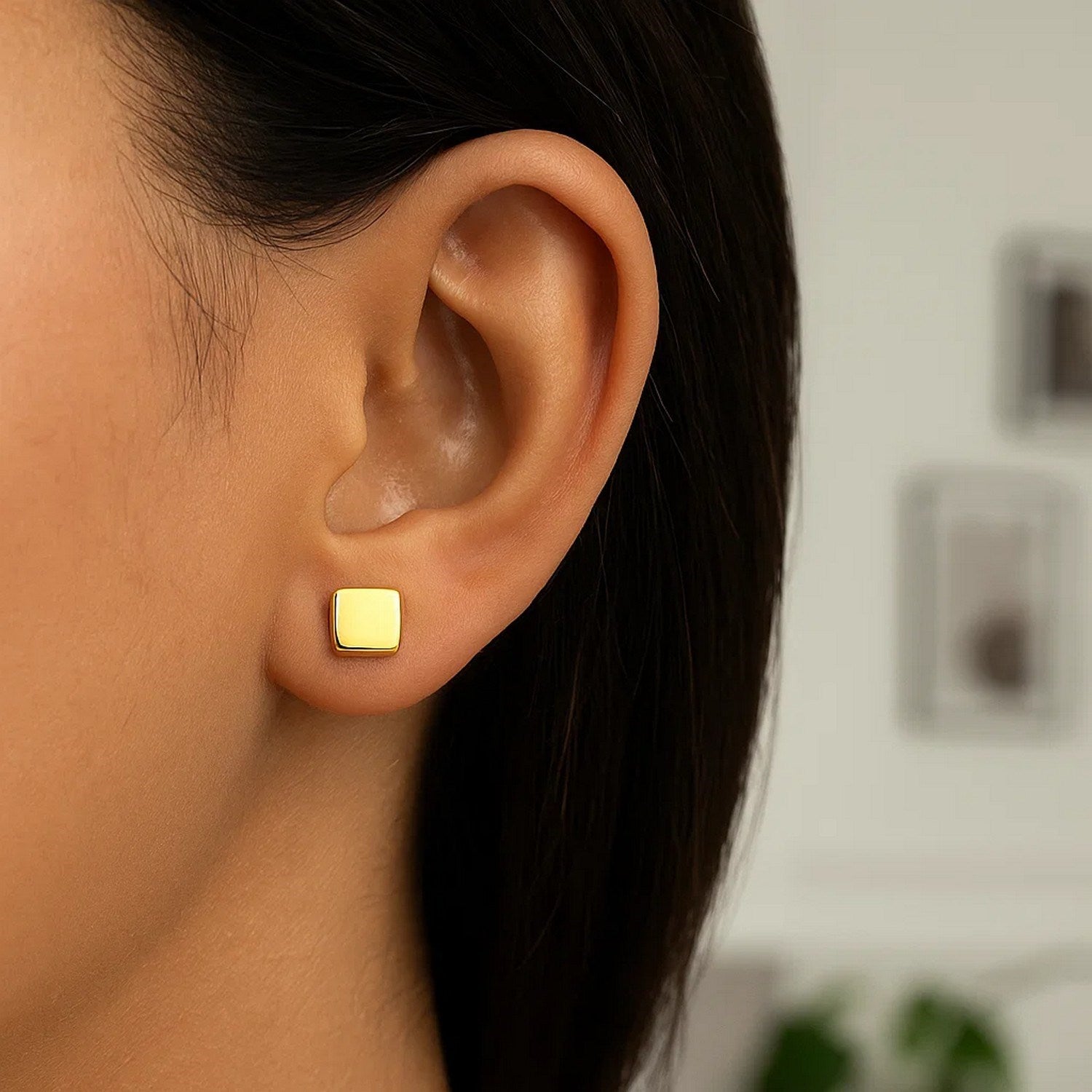 A close-up of an ear wearing a single 14k yellow gold polished cube post earring.