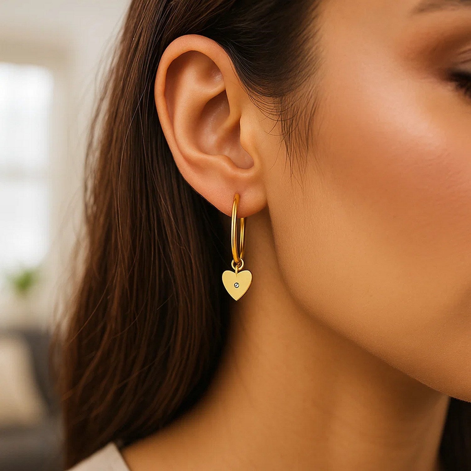 14K yellow gold hoop earrings with a diamond heart charm on a woman's ear.