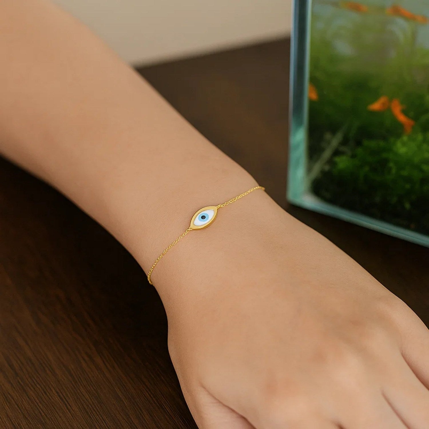 14k yellow gold Mother of Pearl Evil Eye bracelet on a wrist, with a fish tank in the background.
