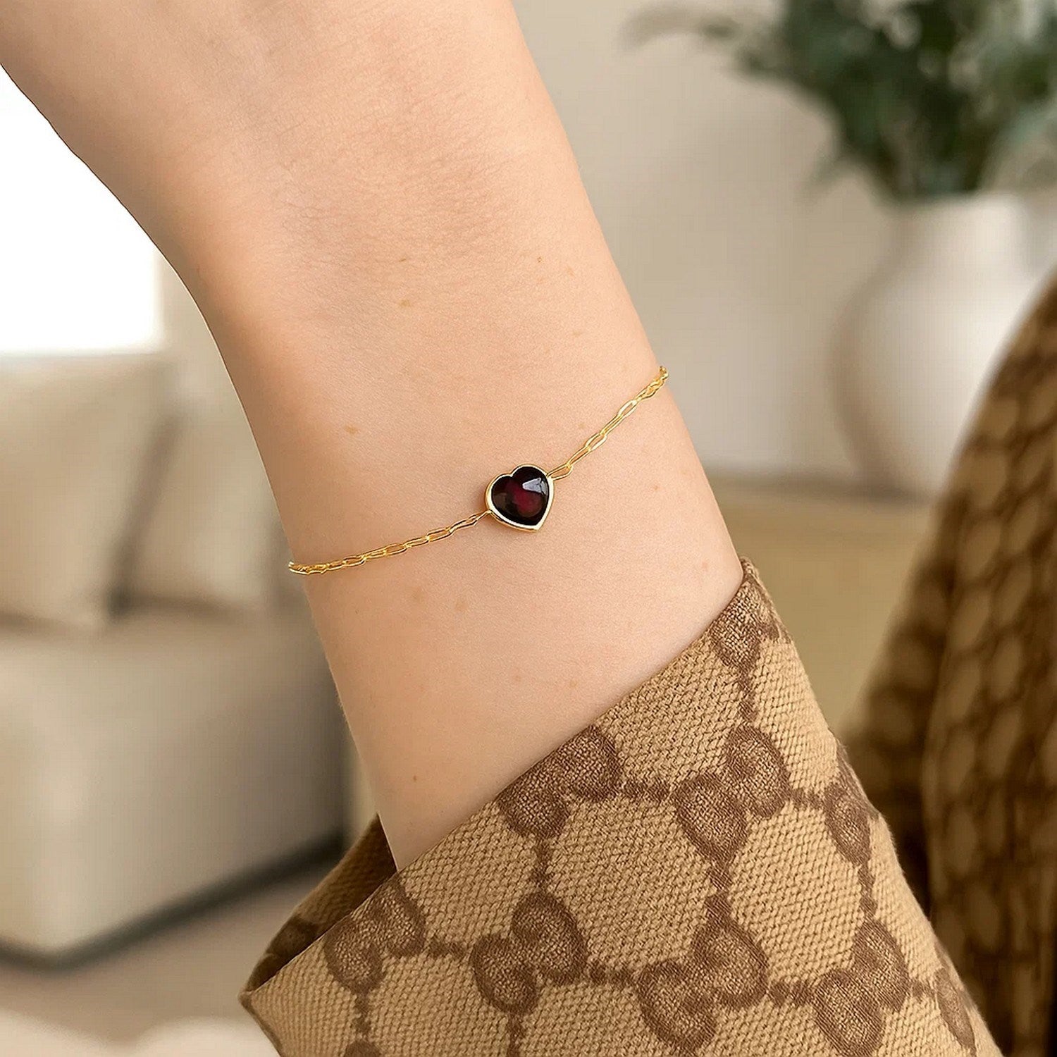 14K yellow gold bracelet with a heart-shaped garnet on a woman's wrist.