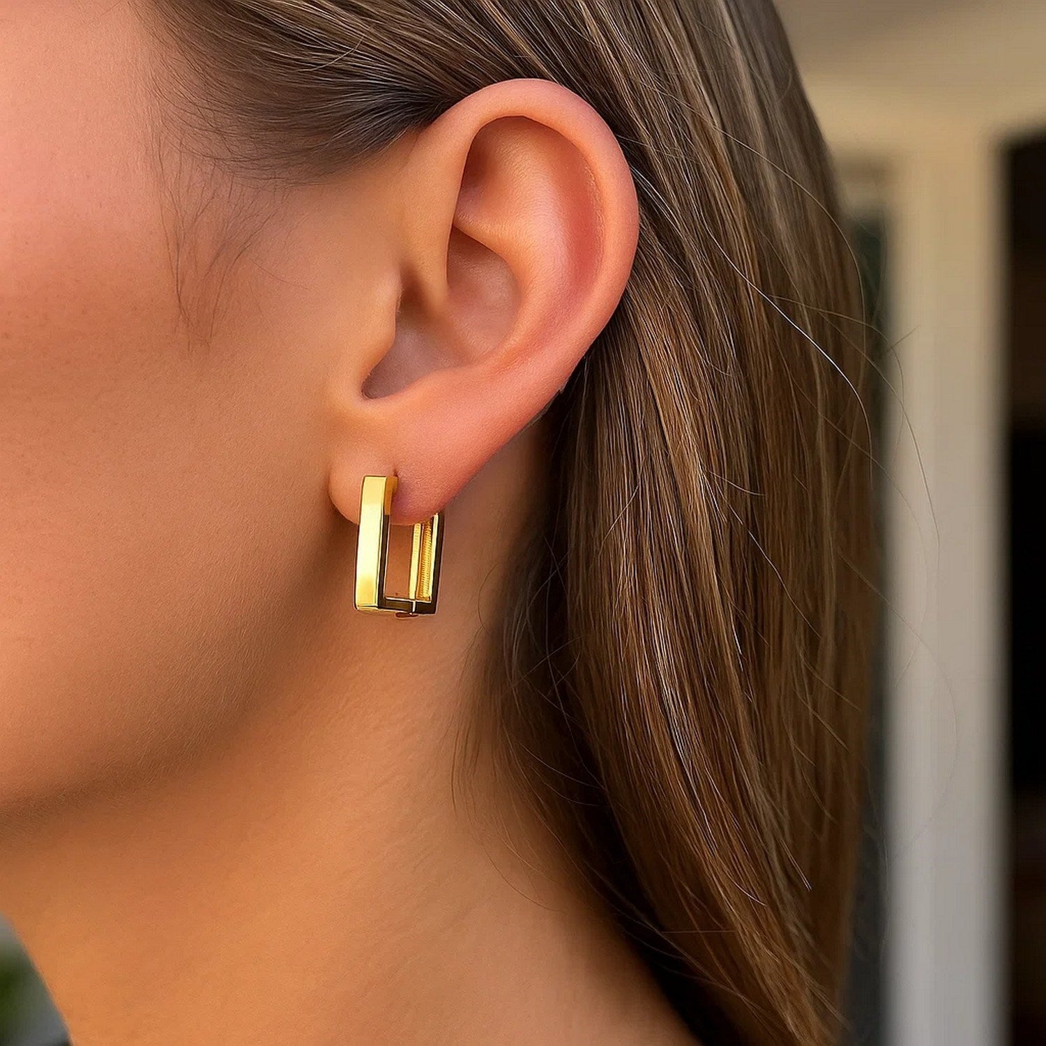 14k yellow gold rectangle huggie hoop earrings on a woman's ear.