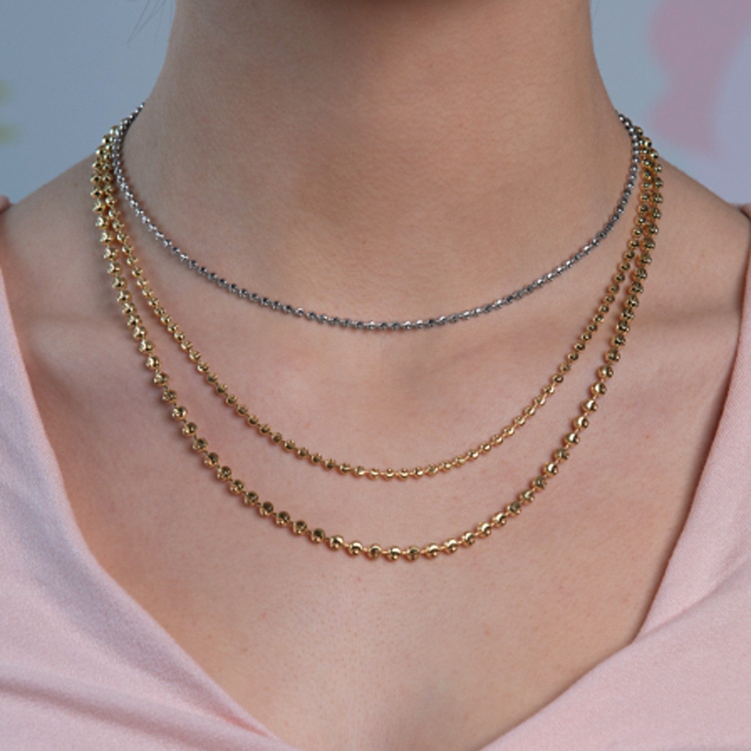 Three layered necklaces, two gold and one silver, are worn on a person's neck.