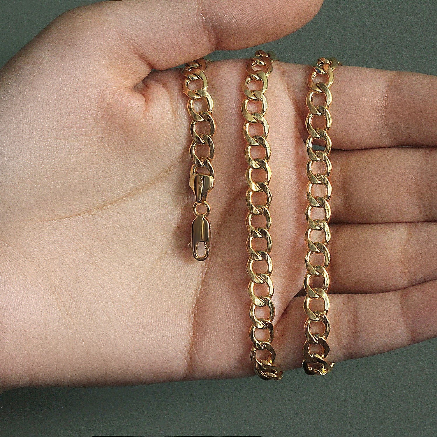 A 10k yellow gold curb chain with a lobster clasp is held in an open palm.