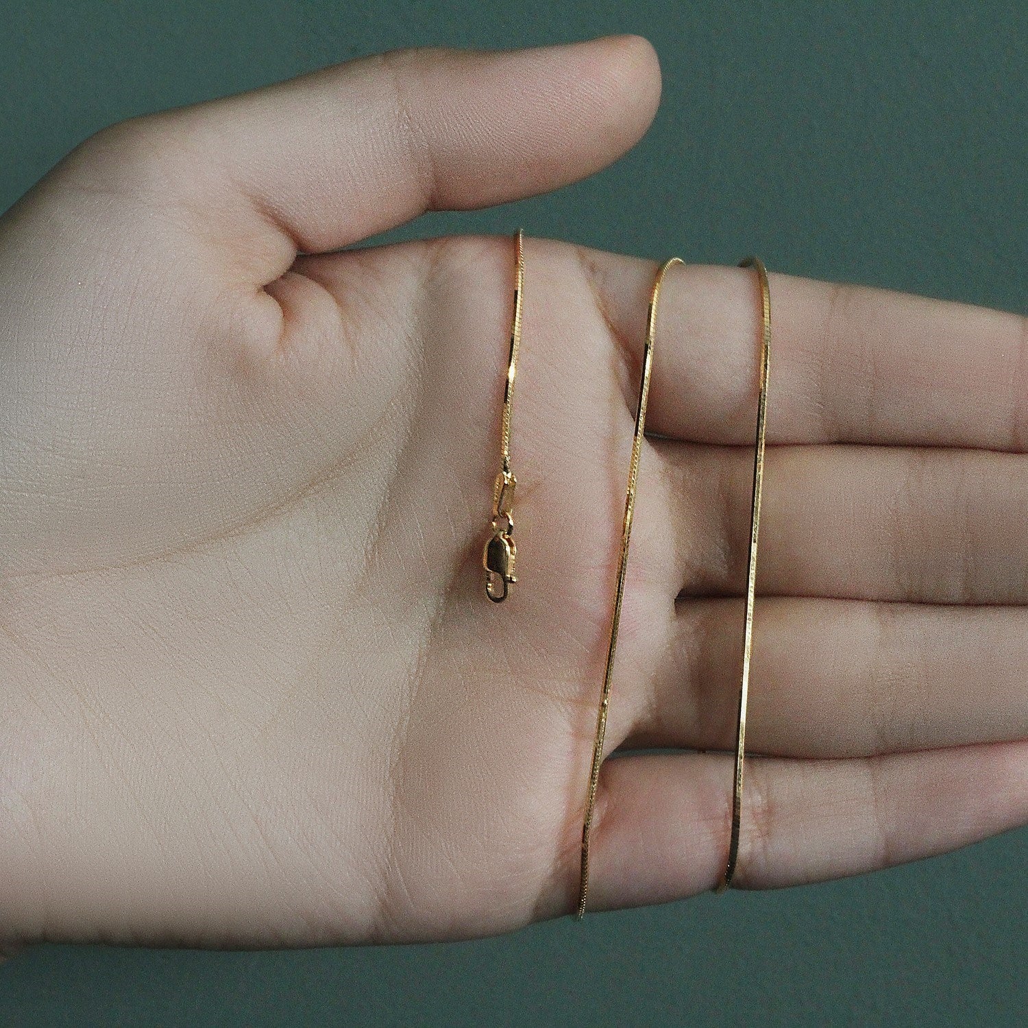 A hand holds a shiny 14K yellow gold octagonal snake chain with a lobster clasp.