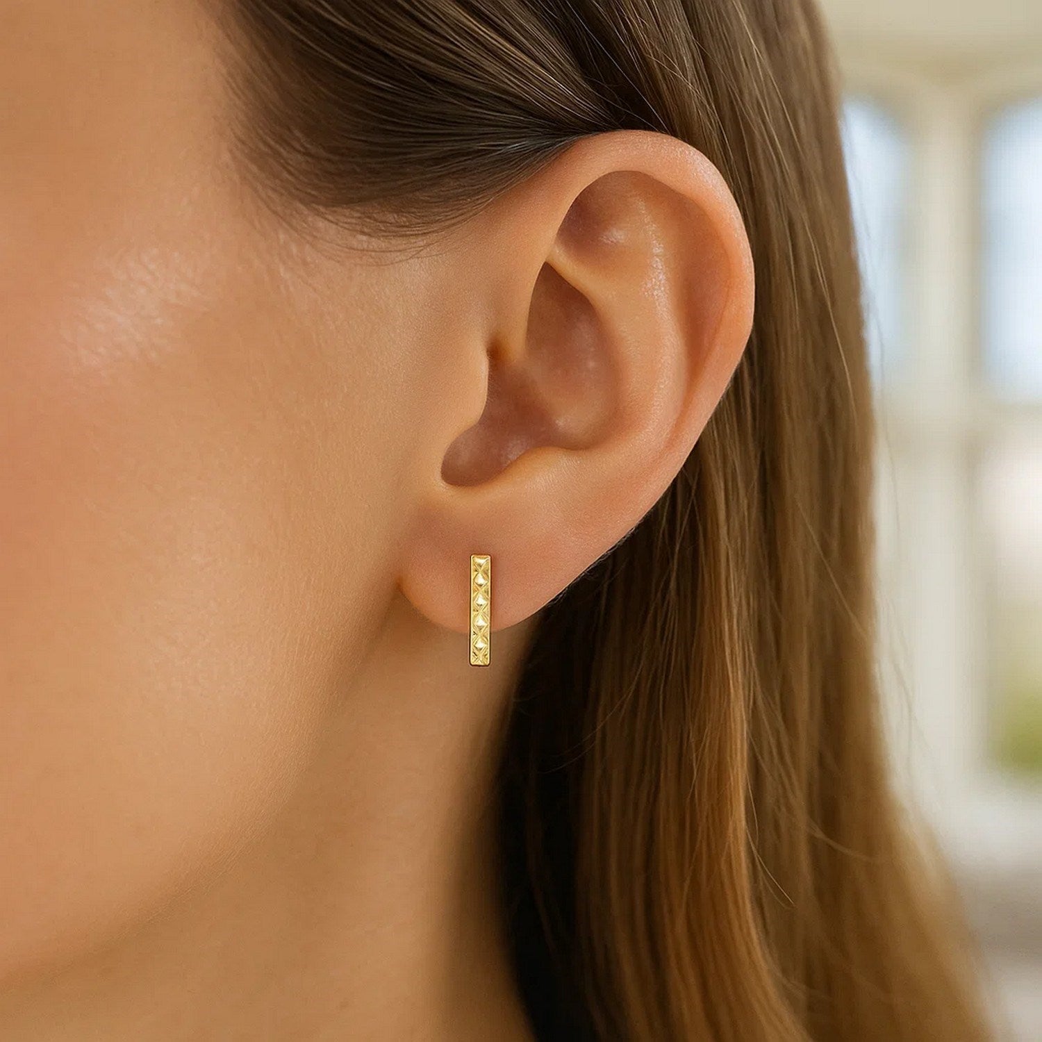 14k yellow gold textured bar earrings on a woman's ear.