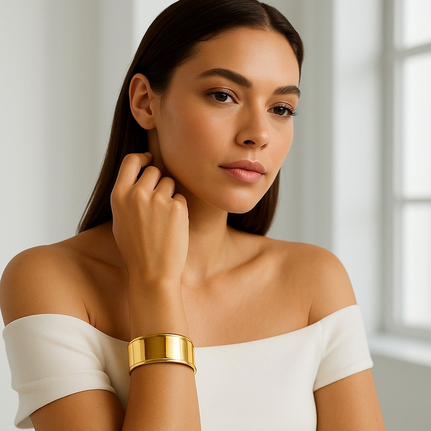 A woman wears a wide, polished 14K yellow gold cuff bangle on her left wrist.