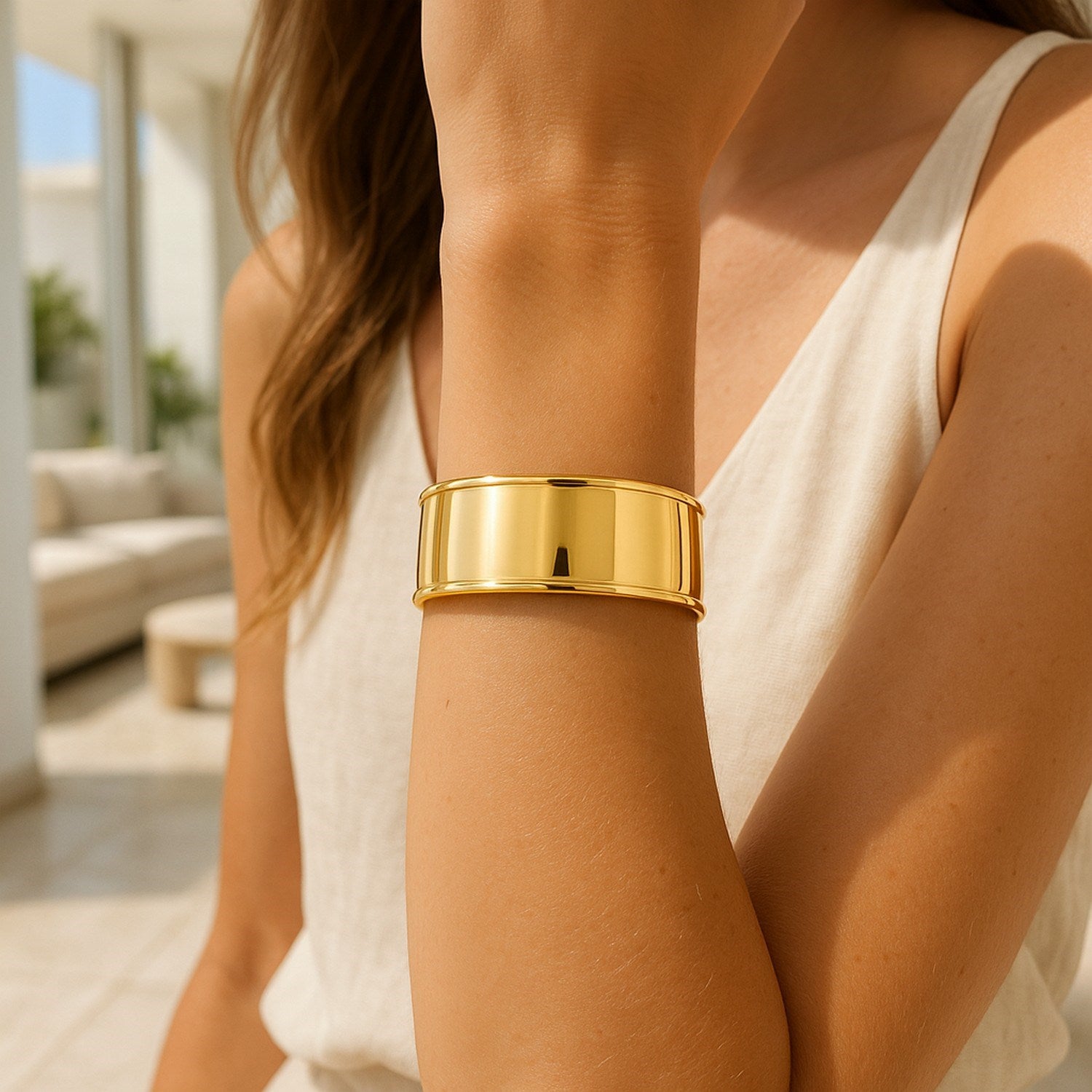A woman wears a wide, polished 14K yellow gold cuff bangle on her right arm.