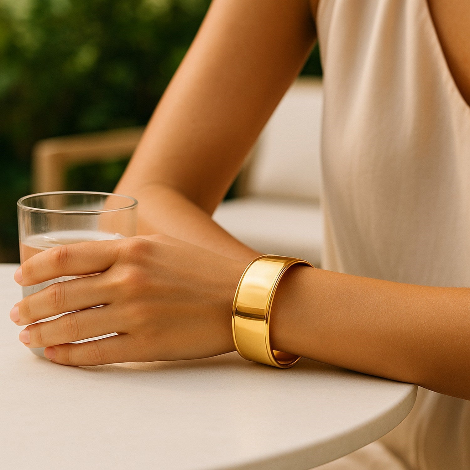 A woman wears a wide, polished 14K yellow gold cuff bangle on her right wrist.