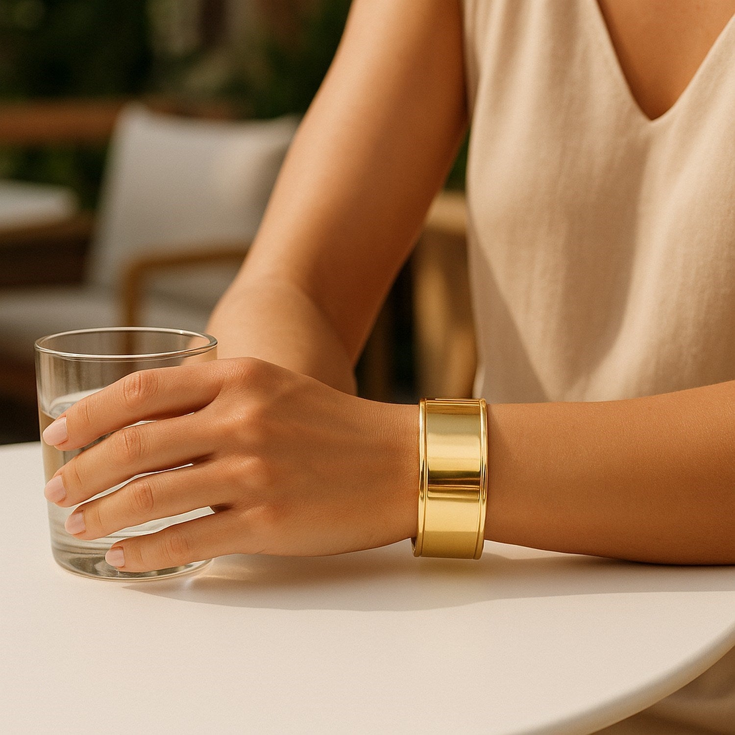 A woman wears a wide, polished 14K yellow gold cuff bangle on her right wrist.
