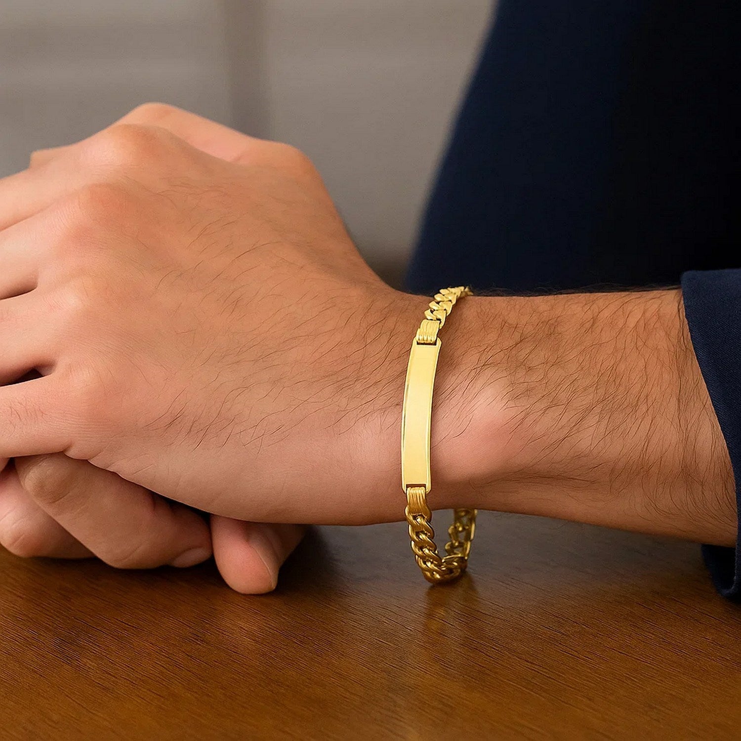A man's arm wears a 14K yellow gold lite Cuban ID bracelet on a wooden table.