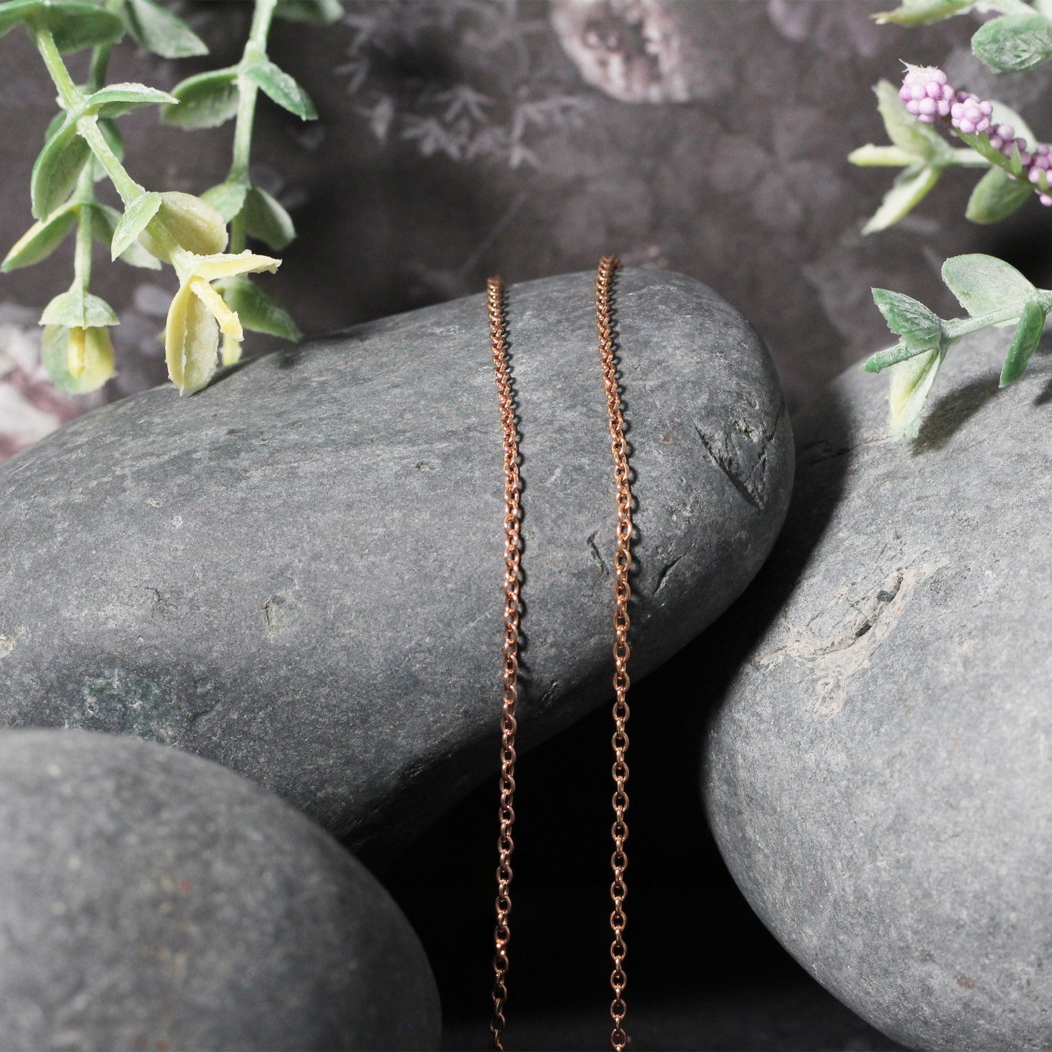 14k rose gold 1.5mm round cable link chain draped over smooth grey stones.