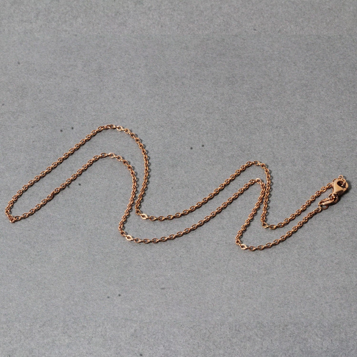 14k rose gold round cable link chain with a lobster clasp on a gray background.