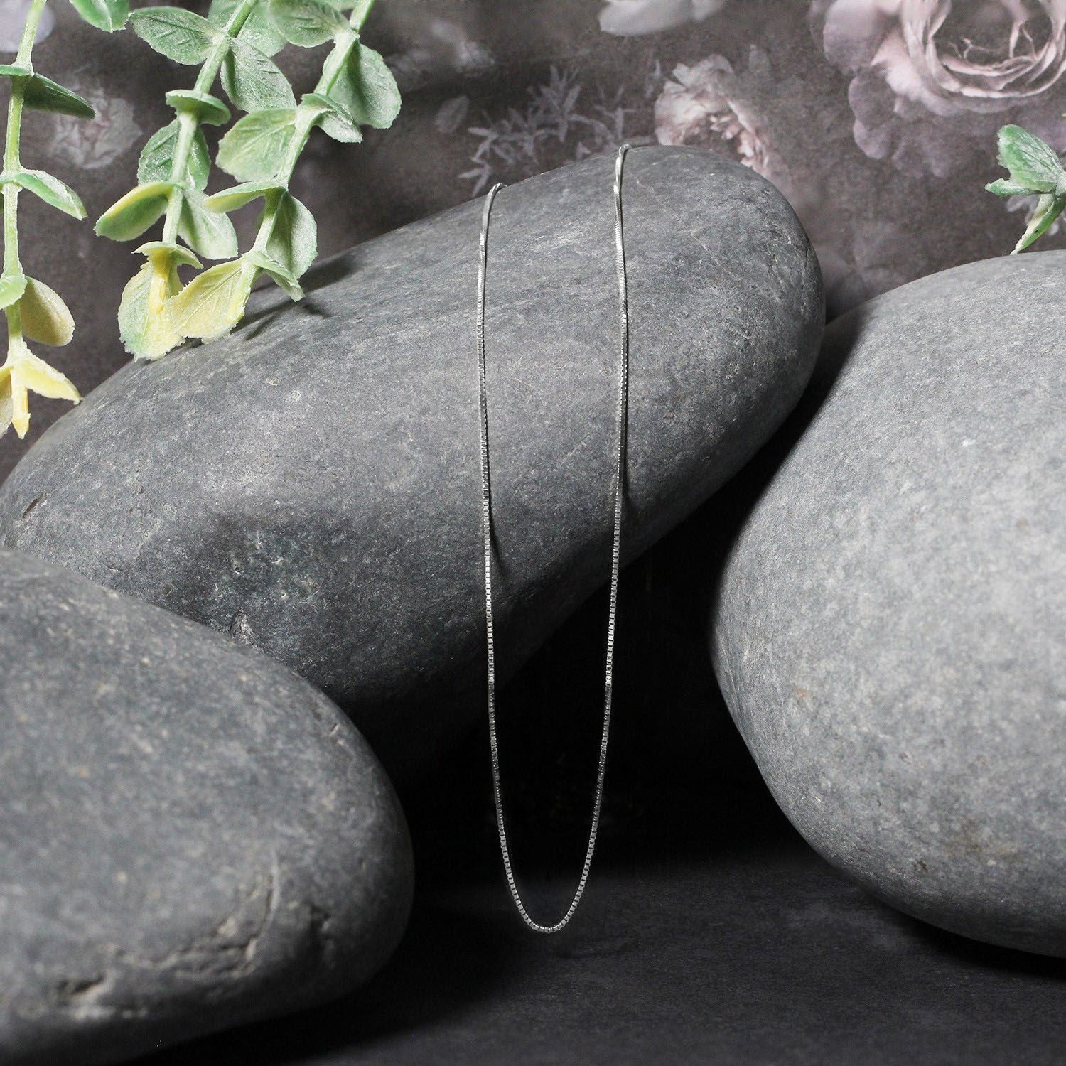 A thin 10k white gold box chain draped over smooth gray stones.