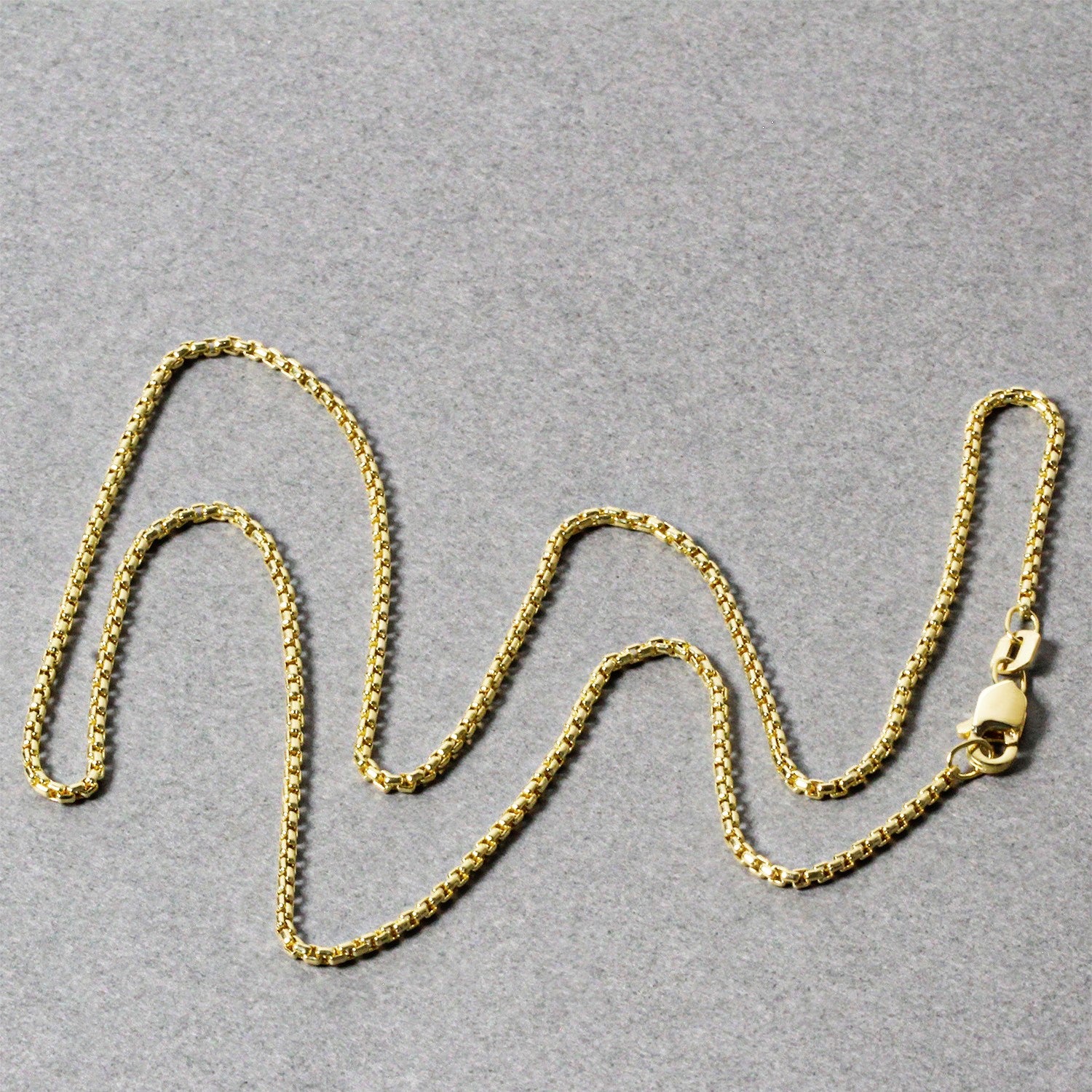 14k yellow gold round box chain with a lobster clasp on a gray background.