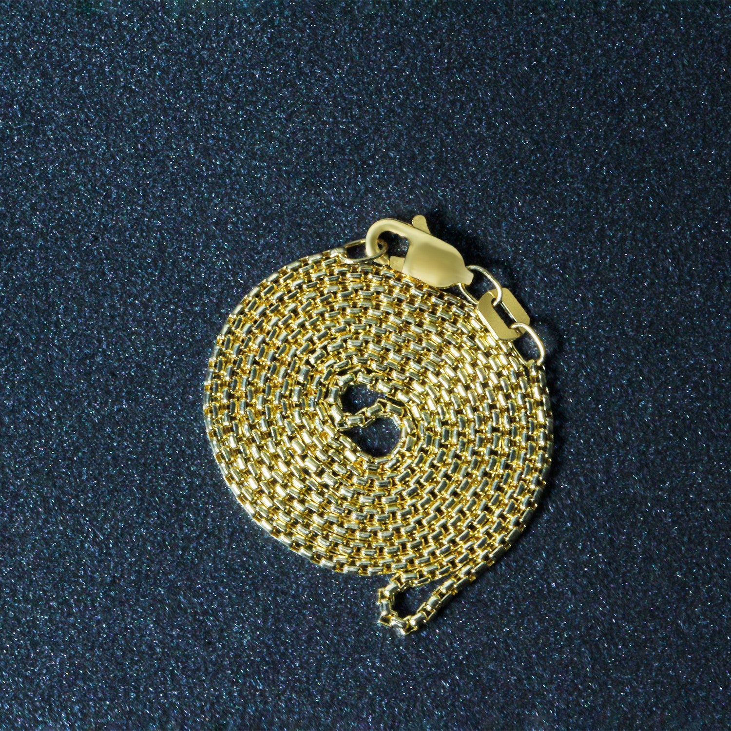 A 14k yellow gold round box chain with a lobster clasp is coiled on a dark, glittery surface.