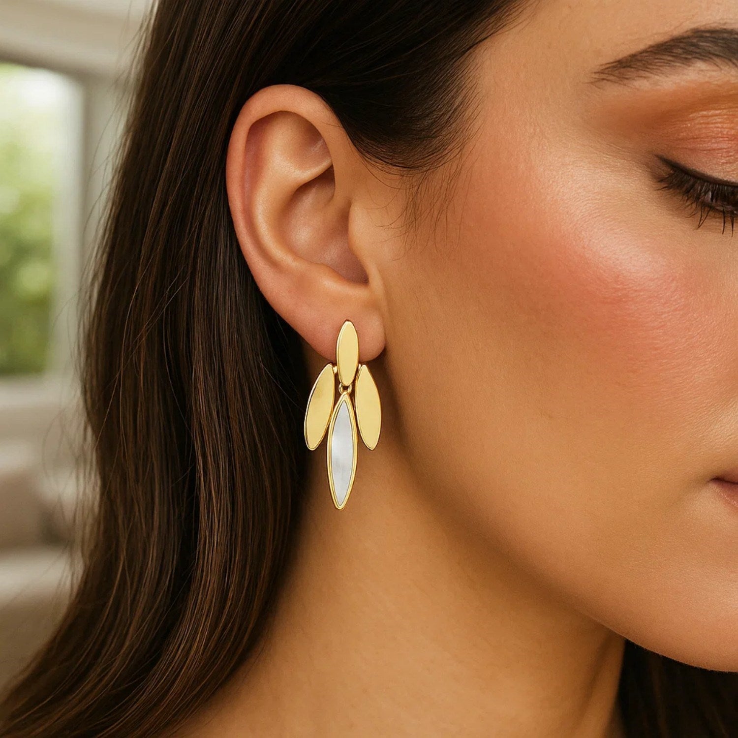 14K yellow gold dangling earrings with mother-of-pearl drops on a woman's ear.