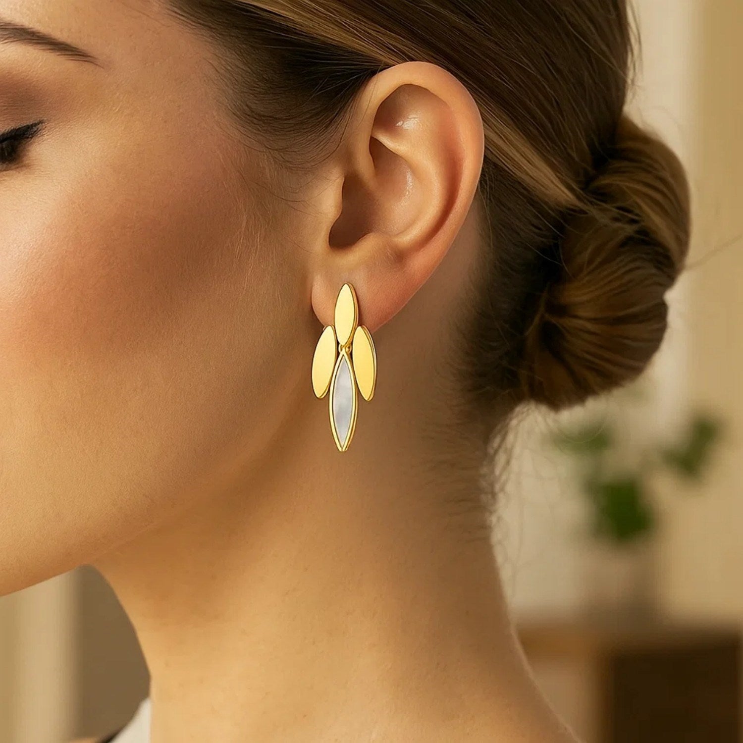 14K yellow gold dangling earrings with mother-of-pearl drops on a woman's ear.
