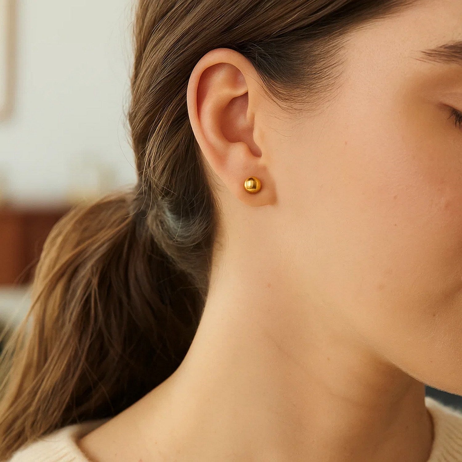 10k yellow gold round stud earrings are worn on a woman's ear.